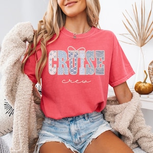 Puede incluir: Una camiseta de color coral con las palabras "CRUISE crew" en una fuente decorativa. La palabra "CRUISE" est&aacute; en un dise&ntilde;o de patchwork con patrones azules y blancos. La camiseta es de estilo casual.