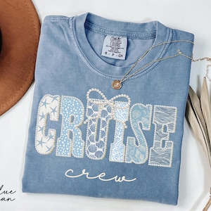 Blue Comfort Colors t-shirt with CRUISE CREW wording in coastal blue patterned varsity letters featuring starfish, shells, waves, and pearl bow accents