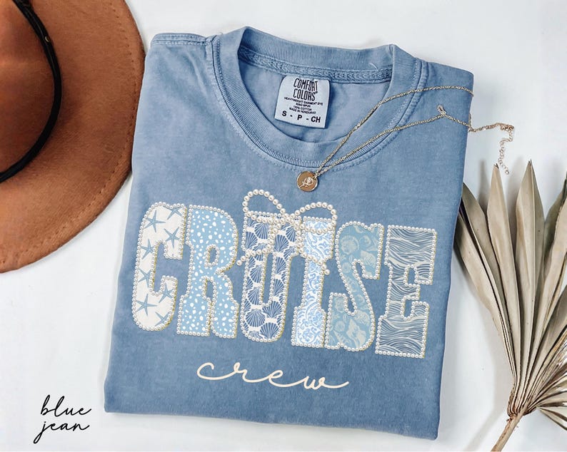 Blue Comfort Colors t-shirt with CRUISE CREW wording in coastal blue patterned varsity letters featuring starfish, shells, waves, and pearl bow accents