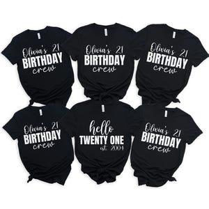 Op de afbeelding: Zes zwarte t-shirts met witte tekst. Vijf shirts lezen "Olivia's 21 BIRTHDAY crew." E&eacute;n shirt zegt "hello TWENTY ONE est. 2004." De shirts zijn gerangschikt op een witte achtergrond.