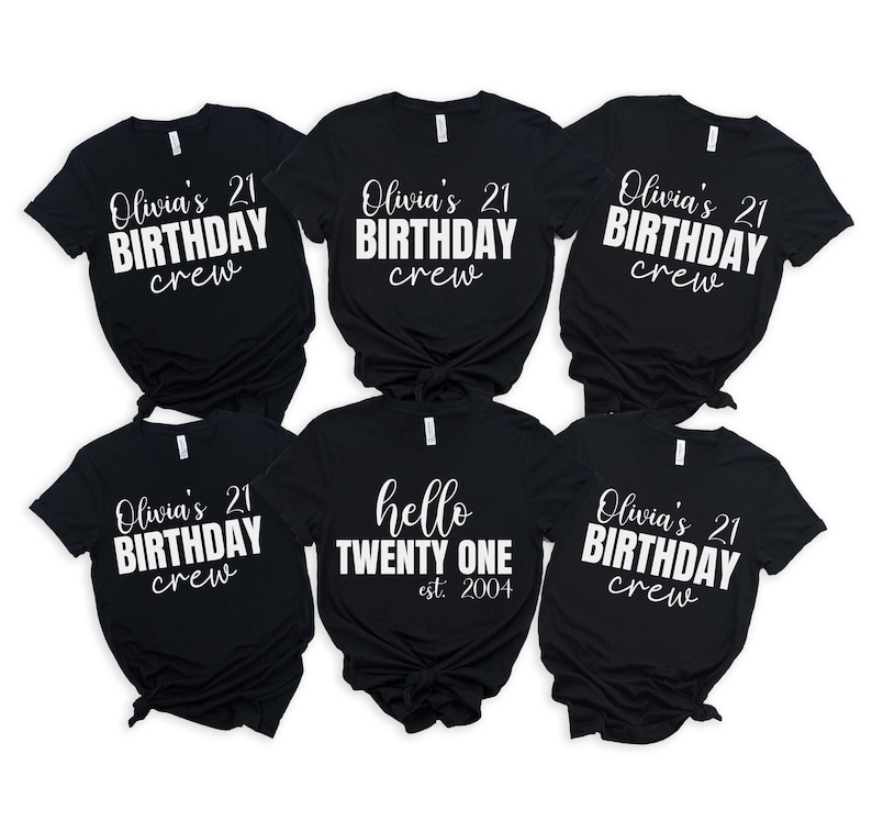 Op de afbeelding: Zes zwarte t-shirts met witte tekst. Vijf shirts lezen "Olivia's 21 BIRTHDAY crew." E&eacute;n shirt zegt "hello TWENTY ONE est. 2004." De shirts zijn gerangschikt op een witte achtergrond.