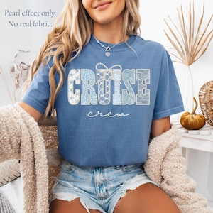 Puede incluir: Una camiseta azul con la palabra "CRUISE" en una fuente decorativa, con varios patrones azules y blancos. Debajo de la palabra "CRUISE" est&aacute; la palabra "crew" en una fuente cursiva. El texto "Pearl effect only. No real fabric." est&aacute; en la esquina superior izquierda.