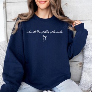 May include: Navy blue sweatshirt with the text "i do all the pretty girls nails" in white script, and a small bow graphic. The sweatshirt is a solid color and has a crew neck.