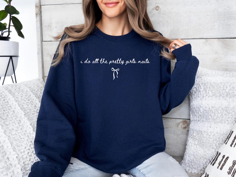 May include: Navy blue sweatshirt with the text "i do all the pretty girls nails" in white script, and a small bow graphic. The sweatshirt is a solid color and has a crew neck.