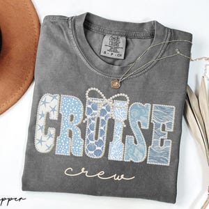 Puede incluir: Una camiseta gris Comfort Colors con las palabras "CRUISE crew" en una fuente decorativa. La palabra "CRUISE" est&aacute; en un dise&ntilde;o n&aacute;utico azul y blanco, y la palabra "crew" est&aacute; en cursiva.