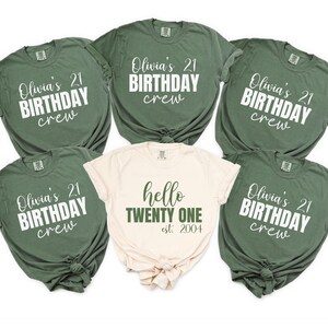 Op de afbeelding: Een verzameling olijfgroene en cr&egrave;mekleurige t-shirts. De meeste shirts hebben de tekst "Olivia's 21 BIRTHDAY crew" in witte letters. E&eacute;n cr&egrave;mekleurig shirt heeft "hello TWENTY ONE est. 2004" in groen. De shirts zijn opgevouwen.