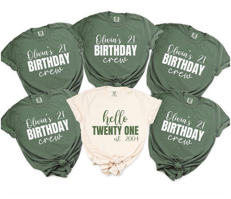Op de afbeelding: Een verzameling olijfgroene en cr&egrave;mekleurige t-shirts. De meeste shirts hebben de tekst "Olivia's 21 BIRTHDAY crew" in witte letters. E&eacute;n cr&egrave;mekleurig shirt heeft "hello TWENTY ONE est. 2004" in groen. De shirts zijn opgevouwen.