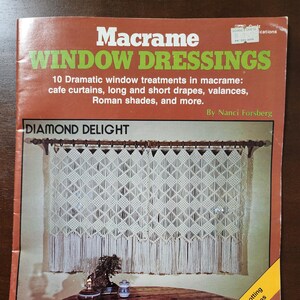 May include: A book cover with the title "Macrame Window Dressings" and a subtitle "10 Dramatic window treatments in macrame: cafe curtains, long and short drapes, valances, Roman shades, and more." The cover features a photo of a white macrame window treatment with a diamond pattern. The book is by Nanci Forsberg.
