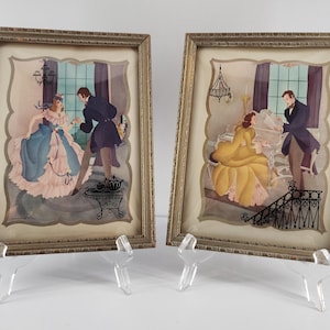 May include: Two framed vintage prints depicting scenes of a couple in period clothing. One print shows a woman in a blue and pink dress, the other a woman in a yellow dress. Both are in gold frames.