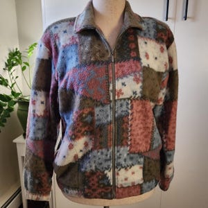 May include: A brown, blue, pink, and white patchwork fleece jacket with a zipper closure.