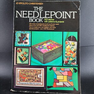 May include: A vintage book titled "The Needlepoint Book" by Jo Ippolito Christensen. The cover features needlepoint examples, including a teddy bear, flowers, a box, and a pillow. The book promises over 300 stitches and 1000 illustrations.