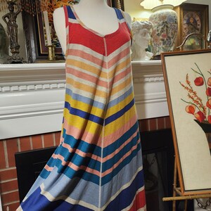 Puede incluir: Un vestido largo a rayas multicolores sobre un maniqu&iacute;. El vestido presenta un patr&oacute;n de chevron con rayas horizontales en tonos rojos, naranjas, amarillos, rosas, azules y grises. Tiene cuello redondo y tirantes.