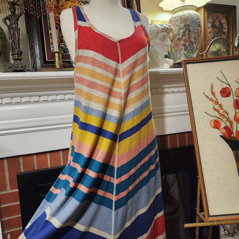 Puede incluir: Un vestido largo a rayas multicolores sobre un maniqu&iacute;. El vestido presenta un patr&oacute;n de chevron con rayas horizontales en tonos rojos, naranjas, amarillos, rosas, azules y grises. Tiene cuello redondo y tirantes.