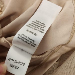 May include: A beige garment interior featuring a white fabric care label with black text. The label displays 'MADE IN INDIA', 'RN#59782', 'Adrianna Papell LLC', '500 Fashion Ave. 10th Floor. New York, USA. NY 10018', 'AP1E200576', and 'IN0007'.