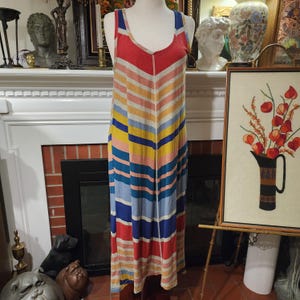 Puede incluir: Un vestido largo sin mangas con un patr&oacute;n de chevron de rayas horizontales en rojo, naranja, amarillo, azul y blanco. El vestido tiene un escote redondo y se muestra en un maniqu&iacute;.