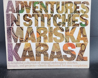 May include: A book cover titled "ADVENTURES IN STITCHES" by Mariska Karasz. The title and author's name are in large, decorative letters with a patterned design. The cover is white with text in various colors, including orange, green, and purple. The book is about embroidery.