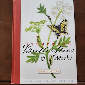 May include: A book cover with a red spine and a white background. The cover features an embroidered image of a butterfly, a caterpillar, and a flower. The title of the book is "STUMPWORK Butterflies & Moths" and the author is "Jane Nicholas". The book is part of the "MILNER CRAFT SERIES".