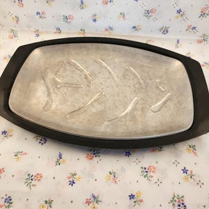 May include: A silver serving tray with a black rim. The tray has a textured surface and is oval shaped.