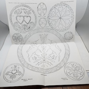 Puede incluir: Libro abierto de diseños de signos hexagonales holandeses de Pensilvania en blanco y negro. Los diseños incluyen corazones, pájaros, flores y formas geométricas. El texto incluye "Double Headed Eagle" y "Unicorn".