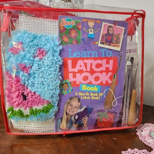 May include: A clear plastic bag containing a latch hook kit. The kit includes a "Learn to Latch Hook" book, a blue and pink latch hook project, and various tools. The book cover is purple with the title in large, bold letters.