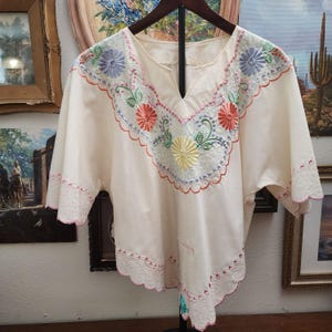 May include: A white ceramic mug with a black handle and the text "But First, Coffee" in a bold, black font. The mug is set against a blurred background, suggesting a cozy setting. The mug appears to be approximately 4 inches tall.