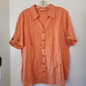 May include: A peach-colored button-down shirt with short sleeves and a textured fabric. The shirt has a collar and a button closure.
