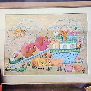 Könnte beinhalten: Gerahmte Stickerei mit einer farbenfrohen Darstellung der Arche Noah. Die Szene zeigt Tierpaare, wie Elefanten, Löwen und Schweine, die auf die Arche zulaufen. Sonne und Wolken sind ebenfalls gestickt.