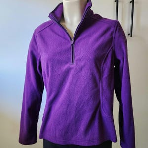 May include: A purple fleece pullover with a quarter-zip closure. The fleece is soft and has a textured look.