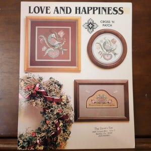 May include: A cross stitch pattern booklet titled "Love and Happiness" with three framed cross stitch designs featuring birds, hearts, and flowers. The booklet is from The Dove's Eye, 3425 Canyon Blvd., Suite 11, Boulder, Co. 80301.