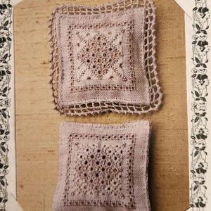 May include: Two square, hand-stitched doilies in a light mauve color. Each doily features a central embroidered design with a delicate, openwork border. The top doily has a scalloped edge. The background is a light brown.