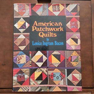 May include: A book titled "American Patchwork Quilts" by Lenice Ingram Bacon. The cover features a colorful patchwork quilt design with various geometric shapes and patterns.