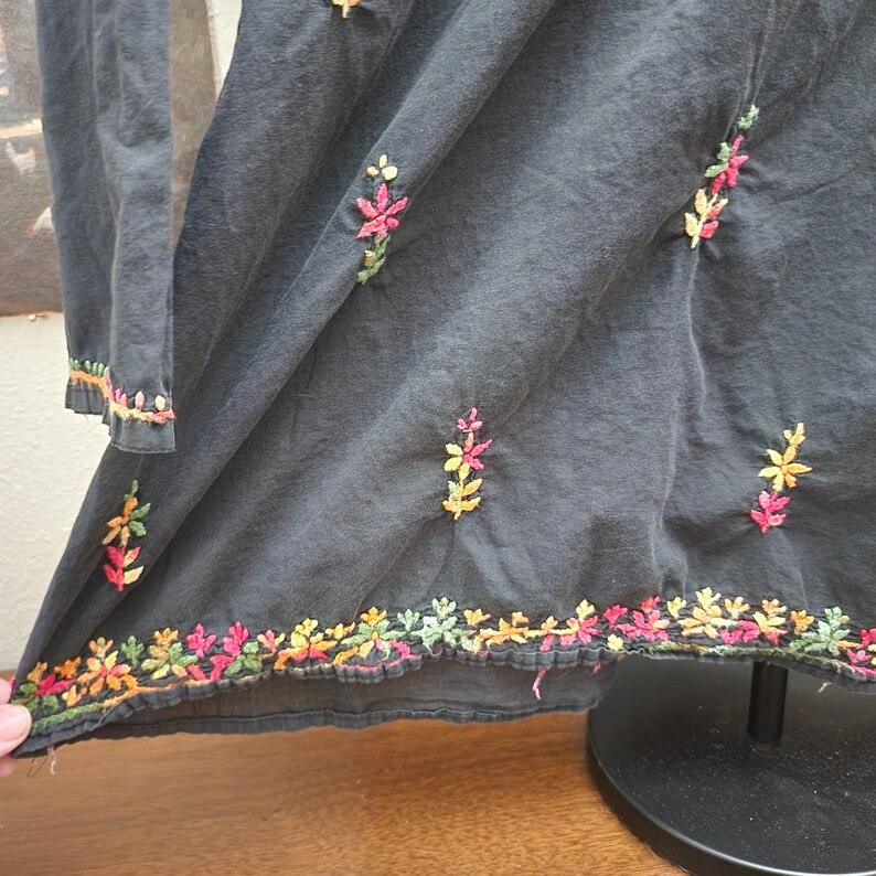 Peut inclure: Robe &agrave; manches longues gris fonc&eacute; avec broderies florales color&eacute;es. La broderie pr&eacute;sente des fleurs roses, jaunes, oranges et vertes. L'ourlet et les poignets des manches sont &eacute;galement brod&eacute;s du m&ecirc;me motif floral. La robe est en tissu doux et fluide.