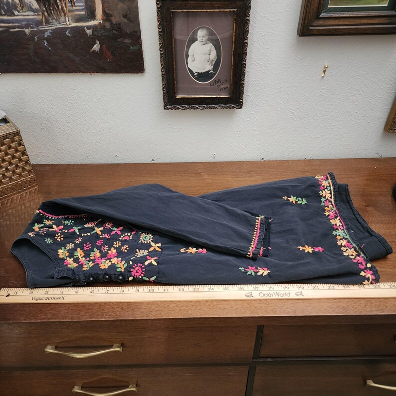 Peut inclure: Haut brod&eacute; bleu fonc&eacute; avec des motifs floraux color&eacute;s. La broderie comprend des fils roses, jaunes, oranges et verts. Le haut est pli&eacute; sur une surface en bois.