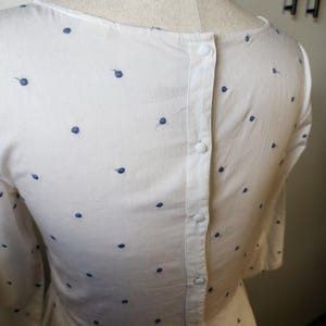 May include: White button-down shirt with a polka dot pattern. The shirt has a button closure down the back.