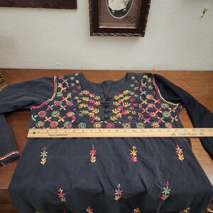 Peut inclure: Une tunique bleu fonc&eacute; &agrave; manches longues avec broderies florales color&eacute;es autour de l'encolure et du corsage. La broderie pr&eacute;sente des fleurs roses, jaunes, vertes et oranges. La tunique a un devant boutonn&eacute; et mesure environ 51 cm de large.