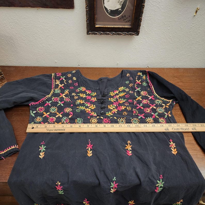 Peut inclure: Une tunique bleu fonc&eacute; &agrave; manches longues avec broderies florales color&eacute;es autour de l'encolure et du corsage. La broderie pr&eacute;sente des fleurs roses, jaunes, vertes et oranges. La tunique a un devant boutonn&eacute; et mesure environ 51 cm de large.