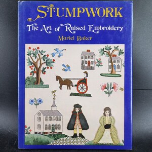 May include: A hardcover book titled "STUMPWORK The Art of Raised Embroidery" by Muriel Baker. The cover features a blue border and a colorful illustration of a horse-drawn carriage, houses, trees, and figures.