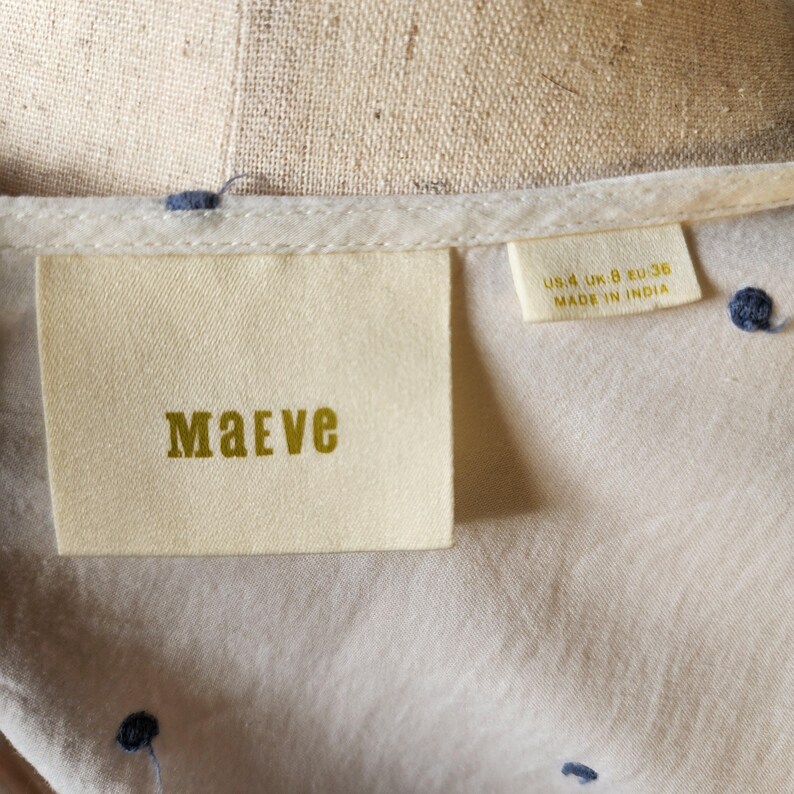 May include: A white cotton shirt with a blue polka dot pattern. The shirt has a label that says "Maeve" and "US 4, UK 8, EU 36, Made in India."