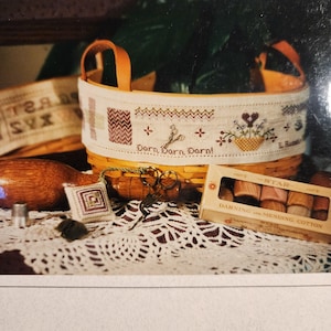 May include: A woven basket with a decorative stitched band featuring a floral design, scissors, and the text "Darn, Darn, Darn!". Includes a small stitched pillow, scissors, and a box of darning and mending cotton. The basket has leather handles.