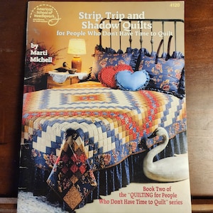 May include: Book cover for "Strip, Trip and Shadow Quilts" by Marti Michell. The book is part of the "Quilting for People Who Don't Have Time to Quilt" series. The cover features a quilt on a bed with a white swan figurine.