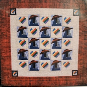 May include: A handmade quilt with a repeating pattern of stylized figures wearing hats and hearts in rainbow colors. The figures are set against a light blue background, framed by a white border and a red outer border.