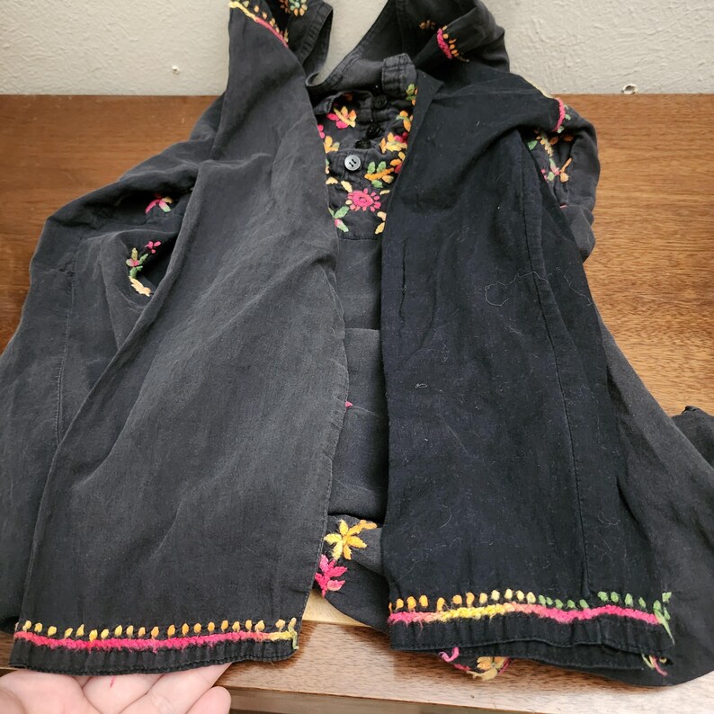 Peut inclure: Veste noire brod&eacute;e avec des accents floraux color&eacute;s. La veste pr&eacute;sente un col et des poignets avec des broderies complexes dans les tons de rose, de jaune et de vert. La doublure int&eacute;rieure de la veste a un motif floral.