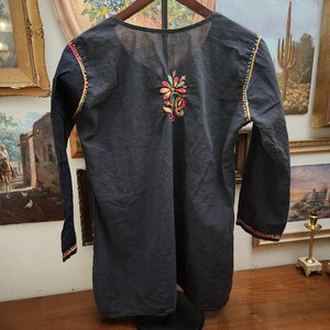 Peut inclure: Une tunique noire &agrave; manches longues et col rond. La tunique pr&eacute;sente des motifs floraux brod&eacute;s color&eacute;s sur la poitrine et le long des poignets et des &eacute;paules. La broderie comprend des nuances de rose, de jaune, de vert et d'orange.