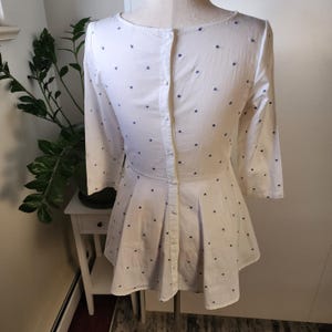 May include: A white dress with a blue polka dot pattern and a button-up back. The dress has a flared skirt and three-quarter sleeves.