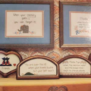 May include: A collection of framed cross-stitch artworks with humorous sayings. One frame reads "When your memory goes... you can forget it!" with an elephant. Another says "You are over the hill..."