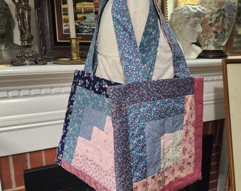 May include: A handmade tote bag with a patchwork design. The bag features a variety of floral and geometric patterns in shades of blue, pink, and navy. The bag has a pink border and matching straps.