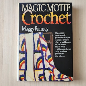 May include: Book cover for "Magic Motif Crochet" by Maggy Ramsay. The cover features a colorful crocheted blanket with rainbow stripes. The book title is in large, bold letters and the author's name is below it. The book description mentions 30 projects using simple geometric shapes to create articles of style and beauty for the home and to wear.