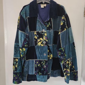 May include: A patchwork jacket in shades of blue, teal, and black, featuring floral and solid fabric squares. The jacket has a corduroy collar, three buttons, and a soft, velvety texture. The floral patterns include yellow and purple flowers.