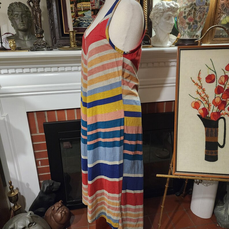 Puede incluir: Un vestido a rayas de colores con cuello en V y tirantes finos. El vestido presenta rayas horizontales en rojo, amarillo, azul y gris. El vestido se exhibe en un maniqu&iacute;.