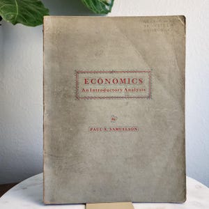May include: A vintage book titled "Economics: An Introductory Analysis" by Paul A. Samuelson. The book cover is beige with red text and a red border.